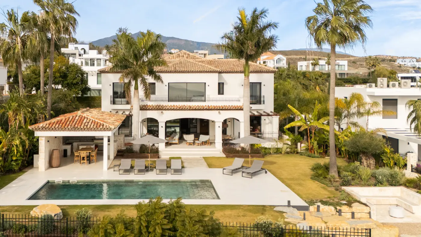 White Andalusian villa with terracotta roof, arched loggia, pool and gardens below the mountains